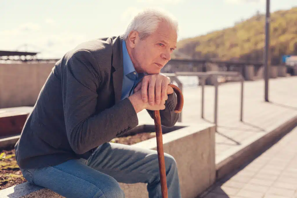 Pleasant white-haired elderly man resting his chin on his hands folded on a cane